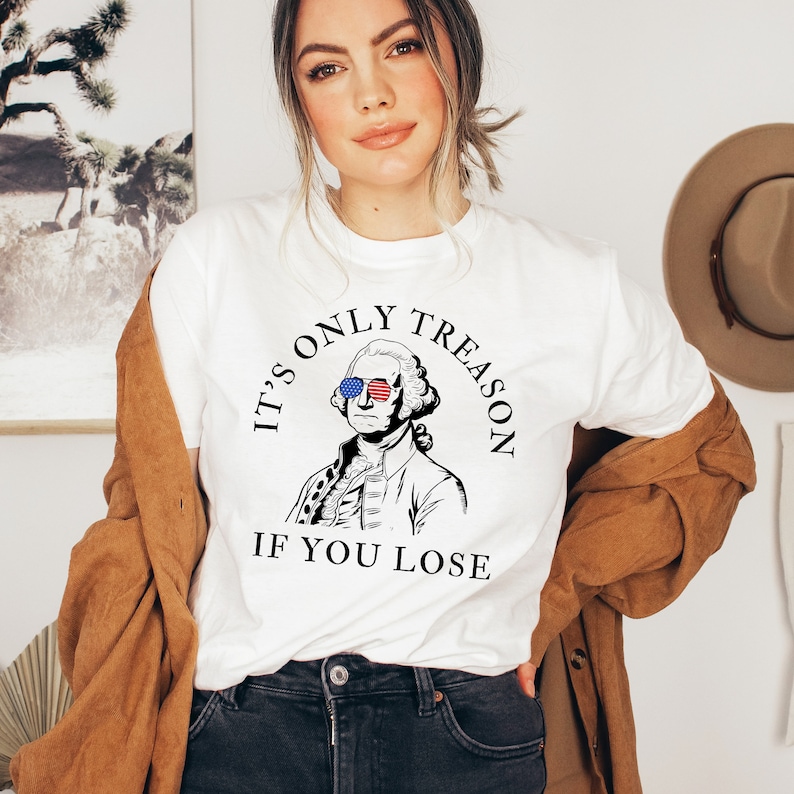 May include: White t-shirt featuring a black and white illustration of George Washington wearing sunglasses with the American flag on them. The text on the shirt reads "It's only treason if you lose."