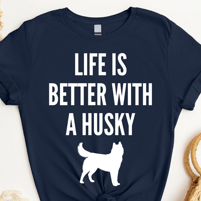 May include: A navy blue t-shirt with white text that reads "Life is better with a husky". A white silhouette of a husky is below the text.