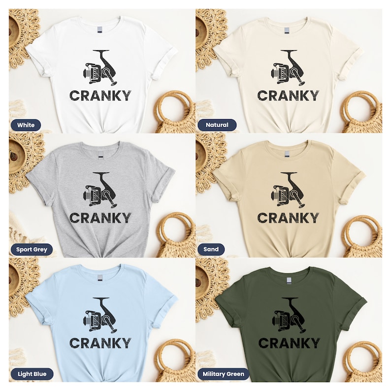 May include: Six different color t-shirts with a black and white graphic of a fishing reel and the word "CRANKY" printed on the front. The colors are white, sport grey, light blue, natural, sand, and military green.