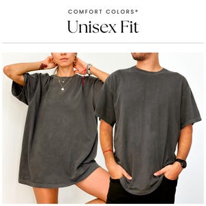 Pu&ograve; includere: Due persone indossano magliette unisex oversize di colore grigio scuro. Le magliette hanno un aspetto vintage e lavato. COMFORT COLORS&reg; Unisex Fit