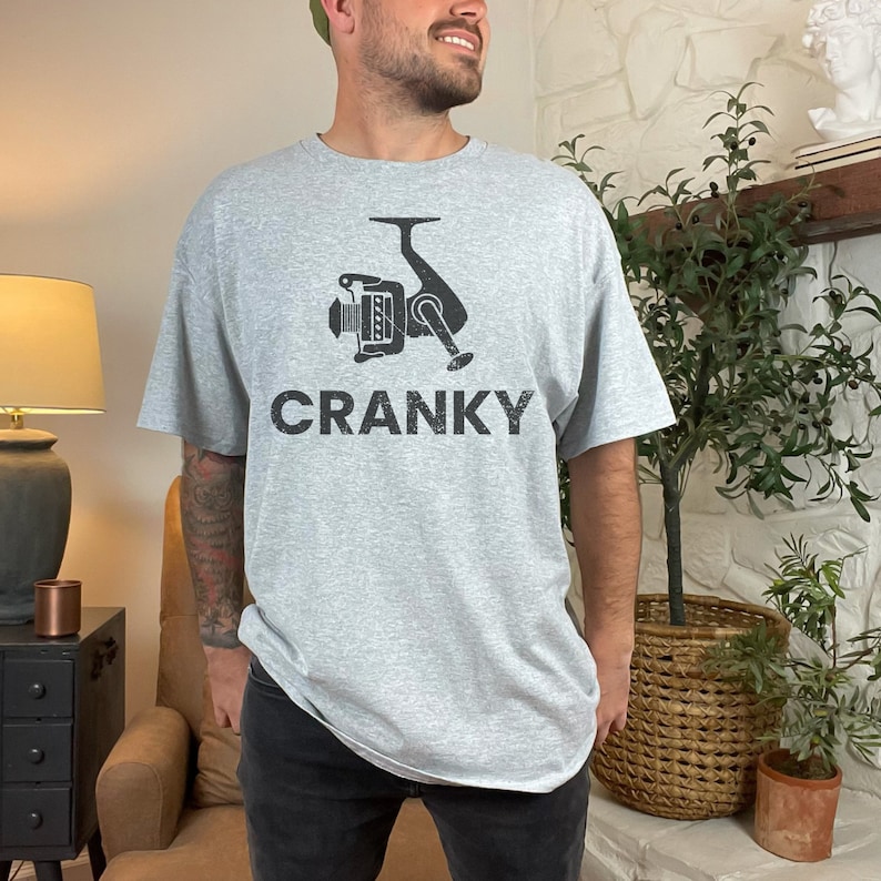 May include: A gray t-shirt with a black graphic of a fishing reel and the word "CRANKY" printed on the front.
