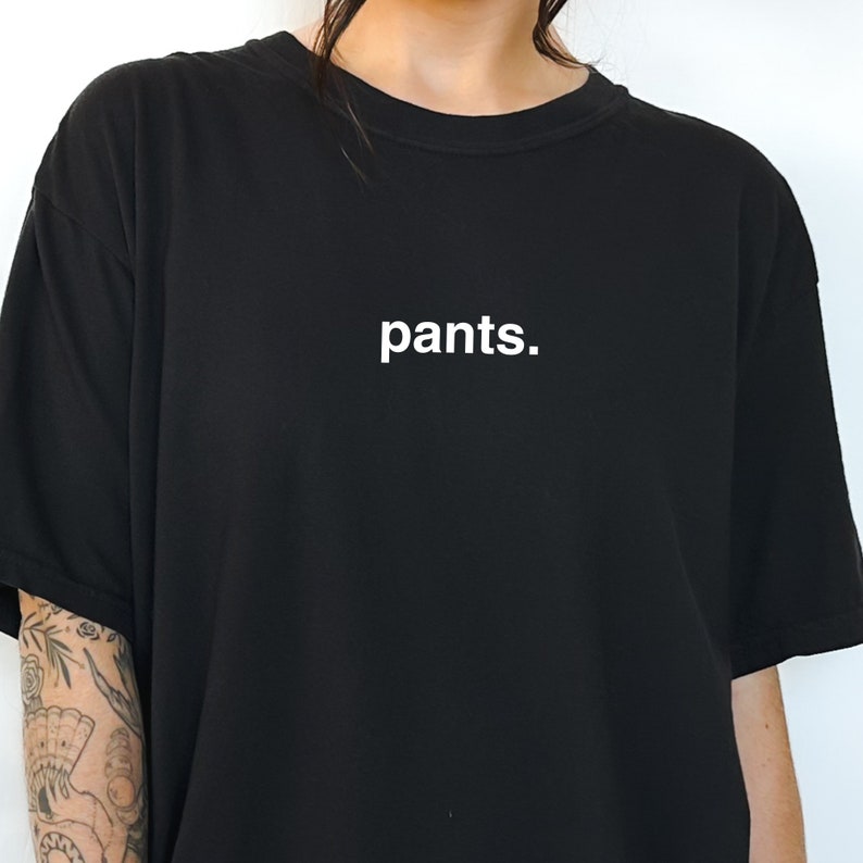 May include: Black t-shirt with the word "pants." printed in white. The shirt has a crew neck and short sleeves. The text is centered on the front of the shirt.