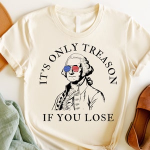 May include: A white t-shirt featuring a graphic of George Washington wearing sunglasses with the American flag design. The text reads "It's only treason if you lose."