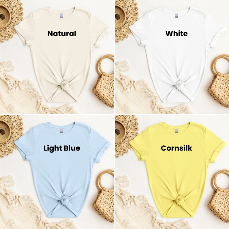 K&ouml;nnte beinhalten: Vier T-Shirts in verschiedenen Farben: Natur, Wei&szlig;, Hellblau und Maisfarbe. Jedes Shirt hat einen andersfarbigen Text auf der Vorderseite: "Natur", "Wei&szlig;", "Hellblau" und "Maisfarbe".