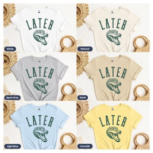 May include: Five different color t-shirts with the text "LATER" in a vintage font and a green alligator graphic. The colors are white, natural, sport grey, sand, and light blue.