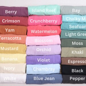 May include: A stack of folded fabric swatches in various colors, including berry, crimson, yam, terracotta, mustard, banana, ivory, white, island reef, crunchberry, watermelon, blossom, orchid, violet, chambray, blue jean, bay, chalky mint, seafoam, light green, moss, khaki, espresso, black, and pepper.
