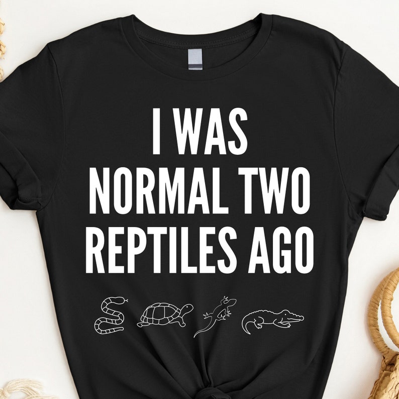 May include: Black t-shirt with white text that reads "I was normal two reptiles ago". The shirt features a line of four white reptile silhouettes: a snake, a turtle, a lizard, and an alligator.