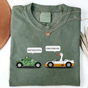 May include: Green t-shirt with a frog in a car and a goose in a car. The frog car says "Beep Beep Bitch" and the goose car says "Honk Honk Hoe".