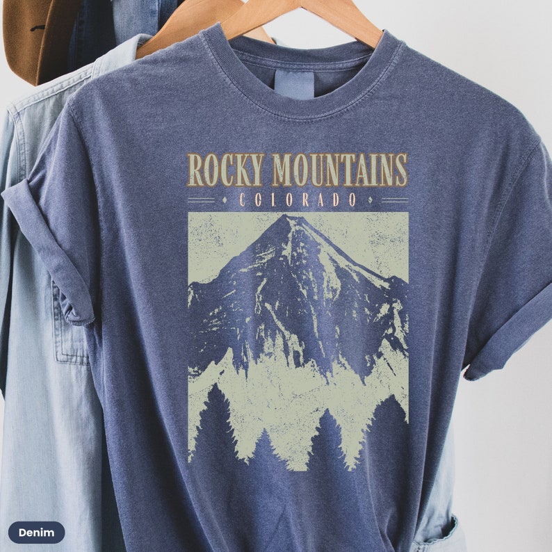 May include: A navy blue t-shirt with a vintage-style graphic of a mountain range and the text "Rocky Mountains - Colorado -" printed on the front.