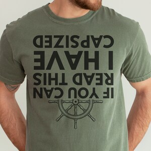 May include: A green t-shirt with a black graphic that reads "If you can read this I have cap sized". The graphic also includes a black steering wheel.