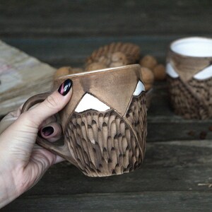 May include: Two brown ceramic mugs with white mountain designs. The mugs have a textured surface and are handmade.