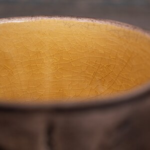 May include: A close-up of the inside of a ceramic bowl with a yellow glaze. The glaze has a crackled finish.