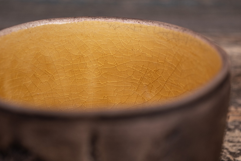 May include: A close-up of the inside of a ceramic bowl with a yellow glaze. The glaze has a crackled finish.