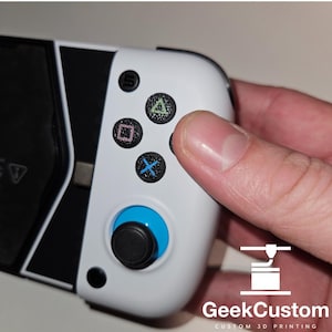 Pode incluir: Um controlador de jogos branco e preto com botões azuis e pretos. O controlador tem um design preto e branco com um botão azul e preto no centro.