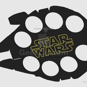Puede incluir: Un objeto negro plano con forma de nave espacial que presenta siete recortes circulares dispuestos en un patrón. El centro del objeto muestra el texto STAR WARS con un contorno amarillo. La silueta general recuerda a una nave espacial.