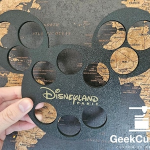 May include: Black metal Disneyland Paris souvenir with six cut-out circles, each revealing a different part of a world map.