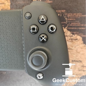 Puede incluir: Un mando de juego negro con una superficie texturizada. El mando tiene un pad direccional, cuatro botones de cara, un joystick y un botón de gatillo. El mando está diseñado para usarse con un dispositivo móvil.