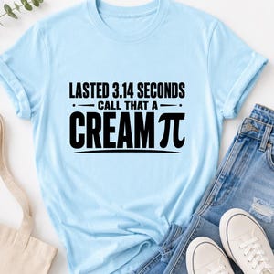 Peut inclure: Un t-shirt bleu clair à manches courtes avec le texte noir "LASTED 3.14 SECONDS CALL THAT A CREAM PI" imprimé au centre, où le symbole mathématique pi remplace les lettres pi dans le mot cream, sur la poitrine du vêtement.