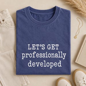 Peut inclure: Un t-shirt bleu marine à col rond avec le texte blanc "LET'S GET professionally developed" imprimé sur le devant. Le vêtement présente des manches courtes, un col standard et une texture de tissu douce avec un aspect légèrement délavé.