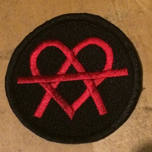 Pode incluir: Um remendo circular preto com um desenho bordado vermelho em forma de coração entrelaçado.