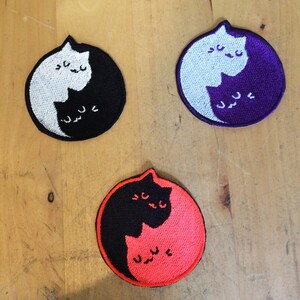 Könnte beinhalten: Drei gestickte Aufnäher mit einem Yin-Yang-Design mit zwei Katzen. Der erste Aufnäher ist schwarz und weiß, der zweite ist lila und weiß und der dritte ist schwarz und orange.