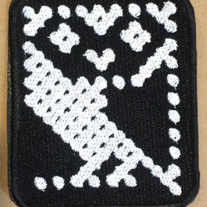 Könnte beinhalten: Schwarz-weiß gestickter Patch mit geometrischem Muster. Der Patch hat einen weißen Rand und ist aus einem weichen, strukturierten Stoff gefertigt.