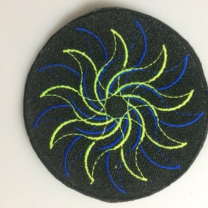May include: A round black patch with a blue and green embroidered spiral design.