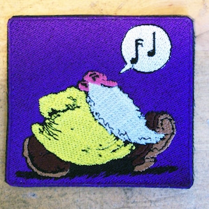 May include: Purple embroidered patch featuring a cartoon character with a yellow coat, white beard, and pink face singing with a musical note above its head. The character is riding a brown and black creature.