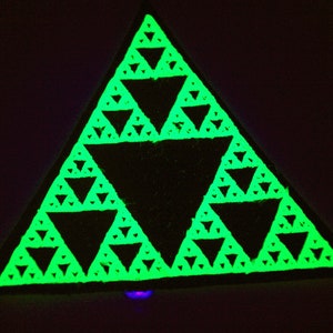 Puede incluir: Un triángulo verde que brilla en la oscuridad con un patrón fractal. El triángulo está formado por triángulos más pequeños que están dispuestos en un patrón repetitivo.