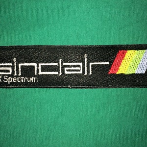 May include: Black and white embroidered patch with the text "Sinclair ZX Spectrum" and a colorful striped design.