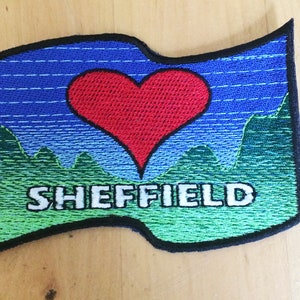 Op de afbeelding: Een blauwe en groene geborduurde patch met een rood hart en de tekst "SHEFFIELD".