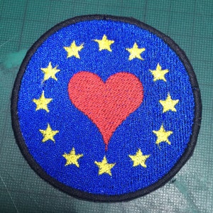 May include: A blue embroidered patch with a red heart in the center and a circle of yellow stars around the heart.