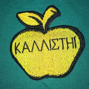 Può includere: Una mela ricamata gialla con contorno nero e la parola "ΚΑΛΛΙΣΤΗΙ" in lettere nere.