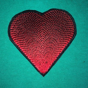 May include: A red heart-shaped patch with a black outline, embroidered with a gradient of red and black stitches. The patch is on a green fabric background.