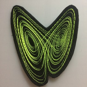 Puede incluir: Un parche bordado negro y verde con forma de mariposa con un patrón de espiral.