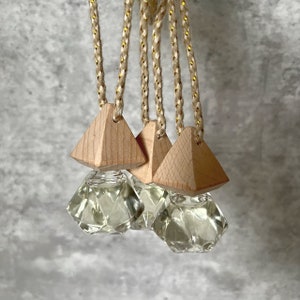 May include: Set of three car air fresheners with diamond-shaped glass bottles and wooden pyramid-shaped tops. The bottles are filled with a clear liquid and the tops are attached to strings.