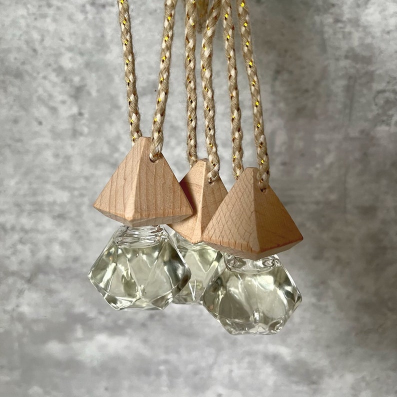May include: Set of three car air fresheners with diamond-shaped glass bottles and wooden pyramid-shaped tops. The bottles are filled with a clear liquid and the tops are attached to strings.