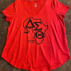 May include: Red t-shirt with a black graphic of a woman's face with an outline of Africa. The graphic includes the Greek letters Delta, Sigma, and Theta.