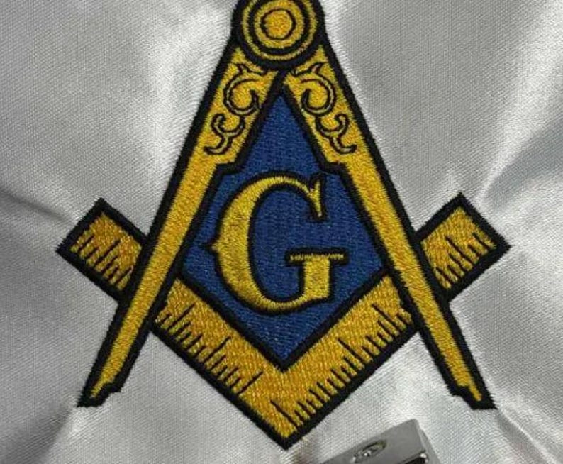 May include: Embroidered Masonic symbol. The design features a yellow square and compass with a blue centre and the letter "G". The symbol is set against a white fabric background.