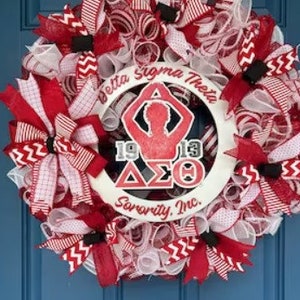 May include: A white wreath with red and white ribbon bows. The wreath has a white circle in the center with the text "Delta Sigma Theta Sorority, Inc." and a silhouette of a person with the letters "1913" and "&Delta;&Sigma;&Theta;" in the center.