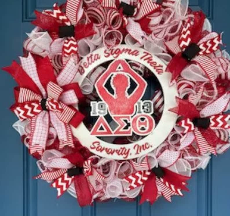 May include: A white wreath with red and white ribbon bows. The wreath has a white circle in the center with the text "Delta Sigma Theta Sorority, Inc." and a silhouette of a person with the letters "1913" and "&Delta;&Sigma;&Theta;" in the center.