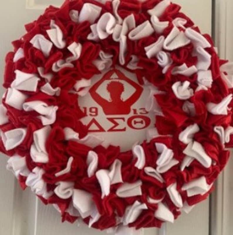 May include: A red and white wreath with a white silhouette of a person with arms raised in the center. The wreath has the text "1919 &Delta;&Sigma;&Theta; 1913" on it.