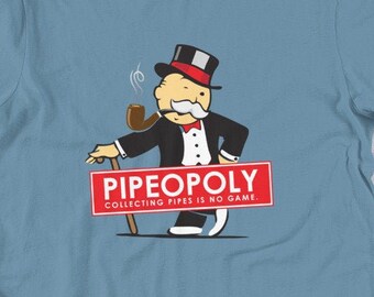 May include: A light blue t-shirt featuring a cartoon illustration of Mr. Monopoly holding a pipe and a cane. The text "Pipeopoly Collecting Pipes is No Game" is printed in red on a white banner.
