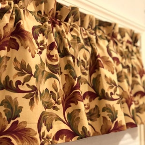 May include: A cream-colored valance with a burgundy and green floral pattern. The valance is gathered and has a ruffled edge.