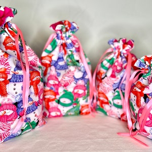 May include: Four drawstring bags with pink ribbon ties. The bags are made of white fabric with a snowman pattern. The snowmen are wearing colorful hats and scarves.