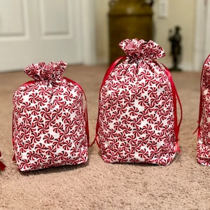 May include: Four red and white candy cane patterned drawstring bags of various sizes. The bags are lined up from smallest to largest.