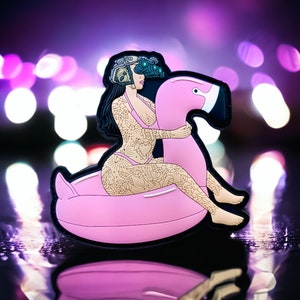 May include: A pink inflatable flamingo pool float with a woman wearing a black bikini and a helmet with goggles sitting on top of it. The background is a blurred purple and white bokeh.