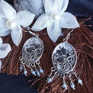 May include: A pair of silver earrings with a black and white patterned design. The earrings are hanging from white fabric flowers with pearl accents.