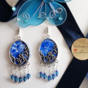 May include: A pair of silver earrings with blue and white patterned oval charms and blue glass beads hanging from the bottom. The earrings are handmade with love.
