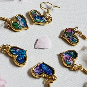May include: Five pairs of gold heart-shaped earrings with a mosaic design. Each earring features a different color combination of blue, green, pink, and white.